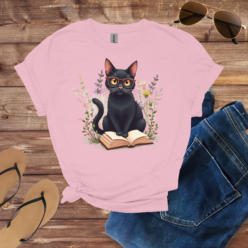 Pink t-shirt with a black cat design on a wooden surface with sunglasses and jeans.