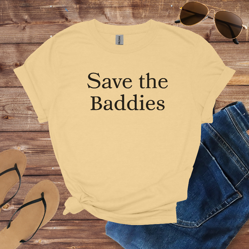 Beige t-shirt with 'Save the Baddies' text on a wooden surface with sunglasses, jeans, and flip-flops.