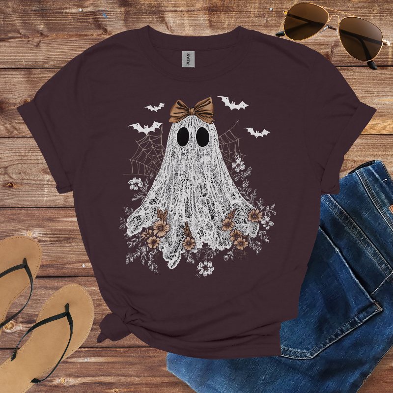 T-shirt with ghost design on a wooden surface with sunglasses, jeans, and sandals.