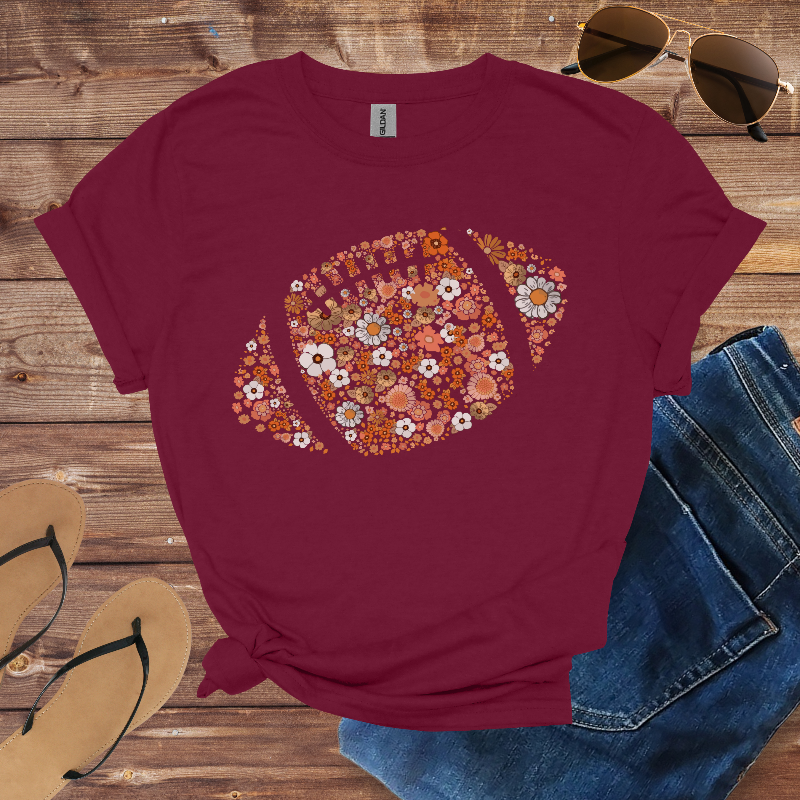 Maroon t-shirt with floral pattern, sunglasses, sandals, and jeans on a wooden surface