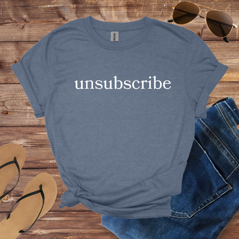Blue t-shirt with 'unsubscribe' text on a wooden surface with sunglasses and sandals.