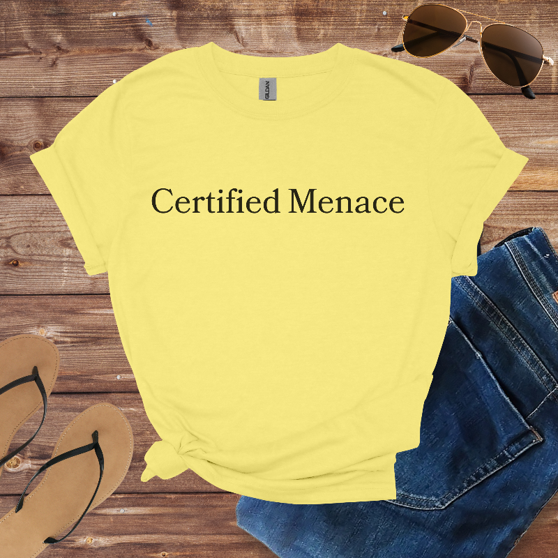Yellow t-shirt with 'Certified Menace' text on a wooden surface with sunglasses, jeans, and flip-flops.