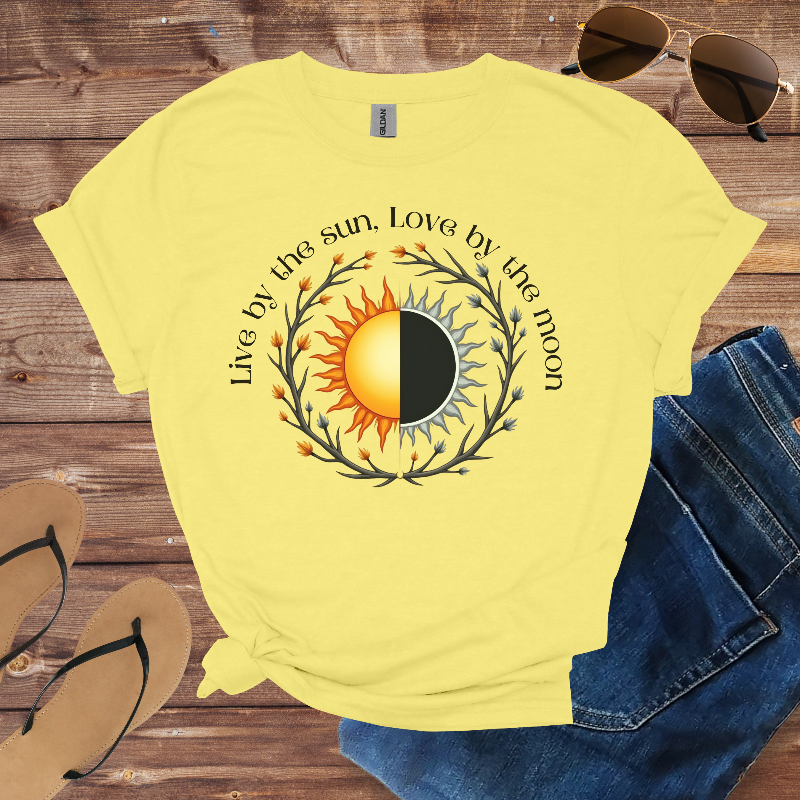 Yellow t-shirt with sun and moon design and text on a wooden surface with sunglasses and jeans.