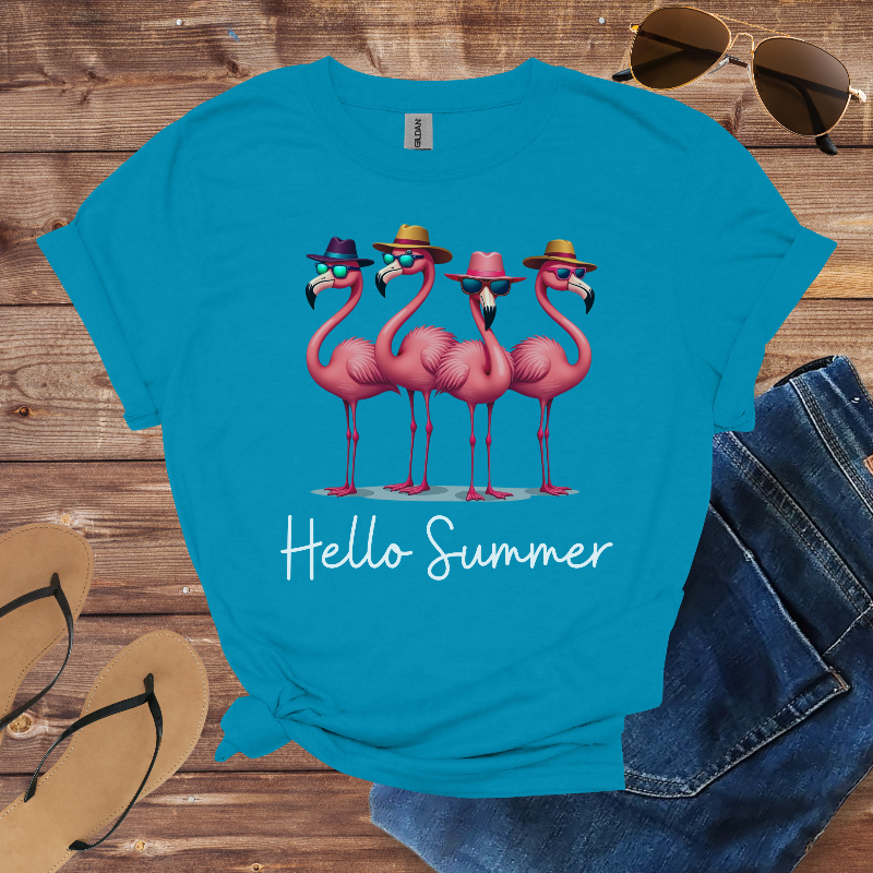 Blue t-shirt with pink flamingo design and 'Hello Summer' text on a wooden surface with sunglasses, jeans, and sandals.