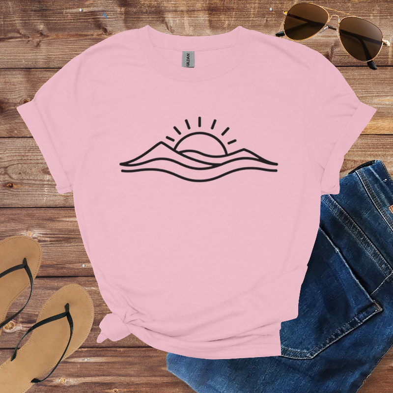 Pink t-shirt with wave and sun design on a wooden surface with sunglasses, jeans, and flip-flops.
