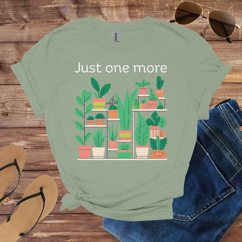 Green t-shirt with plant graphic and text 'Just one more' on a wooden surface with sunglasses, jeans, and sandals.