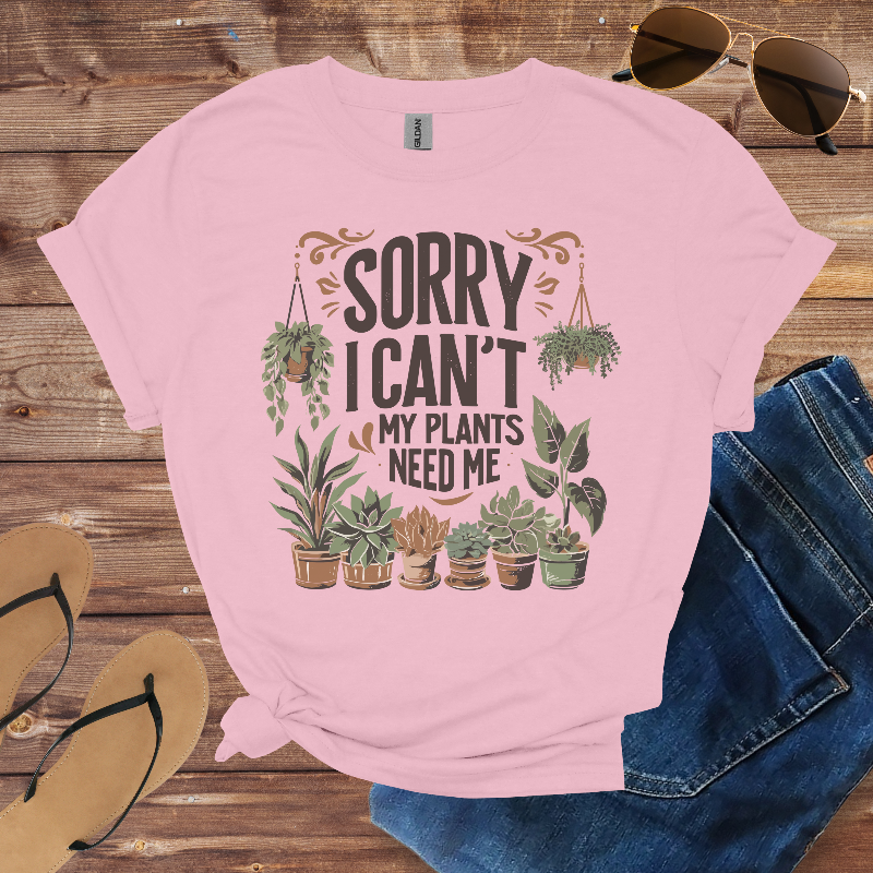 Pink t-shirt with plant-themed design on a wooden surface with sunglasses, jeans, and sandals.