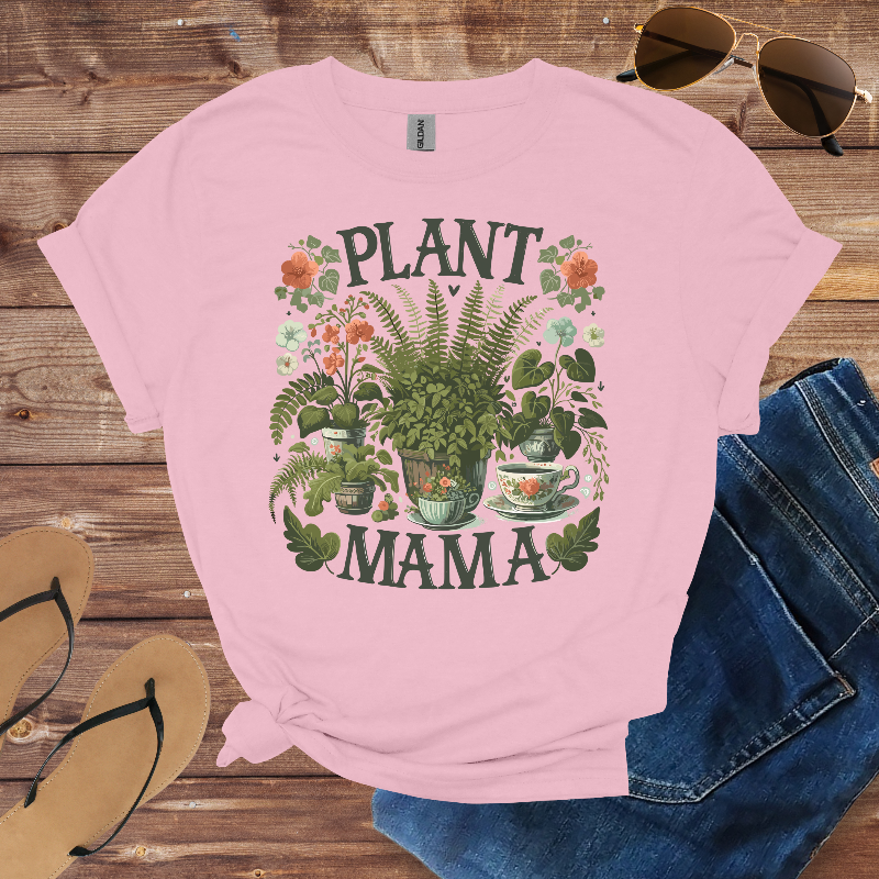 Pink t-shirt with 'Plant Mama' design on a wooden surface with sunglasses, jeans, and sandals.
