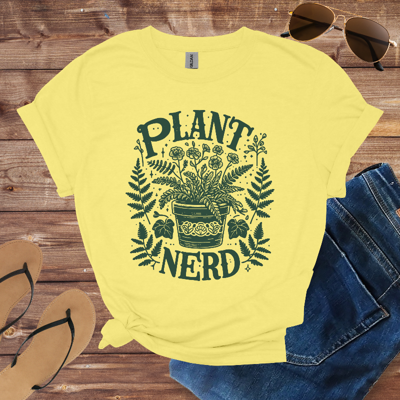 Yellow t-shirt with 'Plant Nerd' design on a wooden surface with sunglasses, jeans, and sandals.
