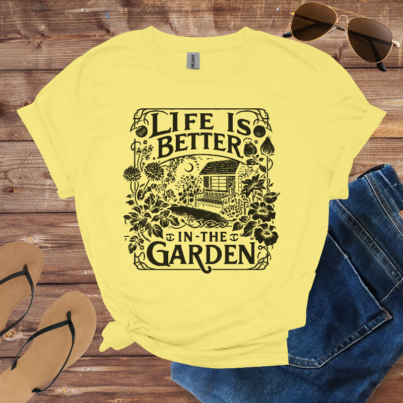Yellow t-shirt with 'Life is Better in the Garden' design on a wooden surface with sunglasses, jeans, and sandals.