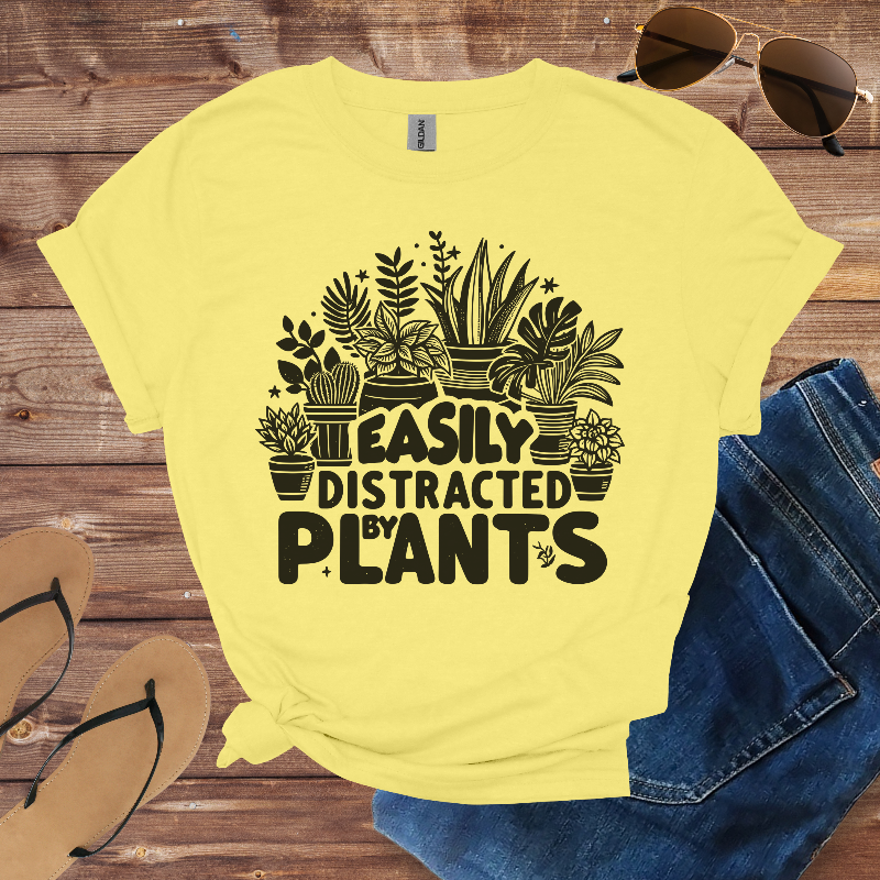 Yellow t-shirt with plant-themed design and text on a wooden surface with sunglasses and jeans.