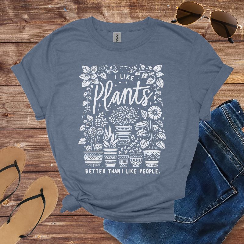 Blue t-shirt with plant-themed design on a wooden surface with sunglasses, jeans, and sandals.