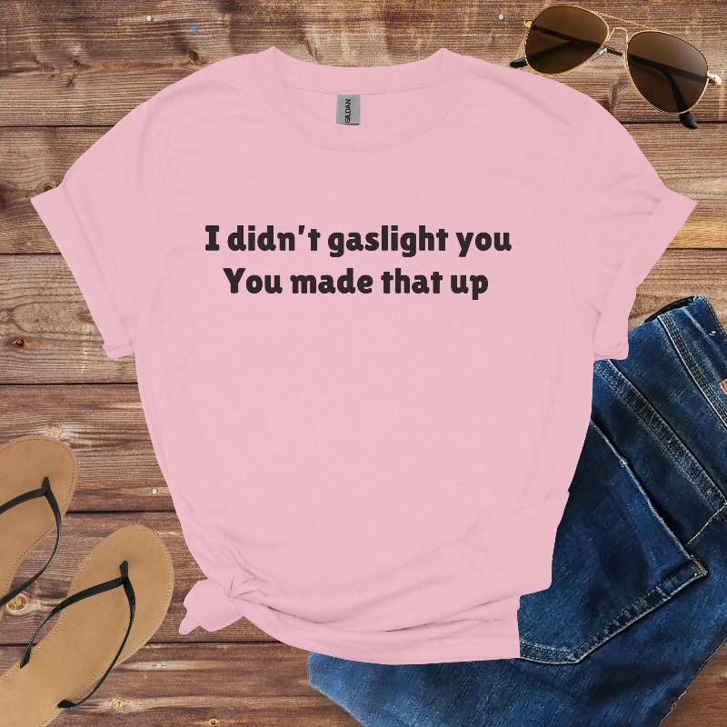 Pink t-shirt with text on a wooden surface with sunglasses, jeans, and sandals.