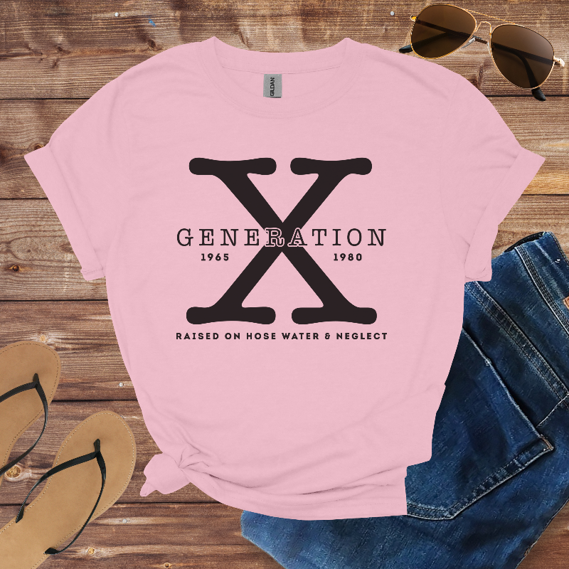 Pink t-shirt with 'Generation X' design on a wooden surface with sunglasses, jeans, and flip-flops.
