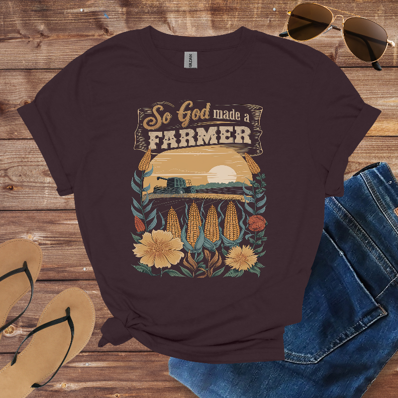 T-shirt with 'So God made a farmer' design on a wooden surface with sunglasses, jeans, and sandals.