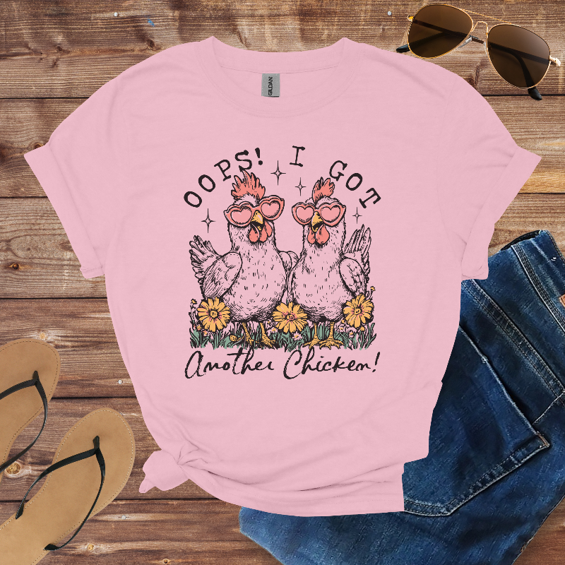 Pink t-shirt with chicken graphic and text on a wooden surface with sunglasses and jeans.