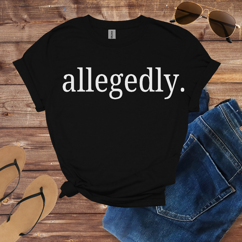 Black t-shirt with 'allegedly.' text on a wooden surface with sunglasses, jeans, and flip-flops.