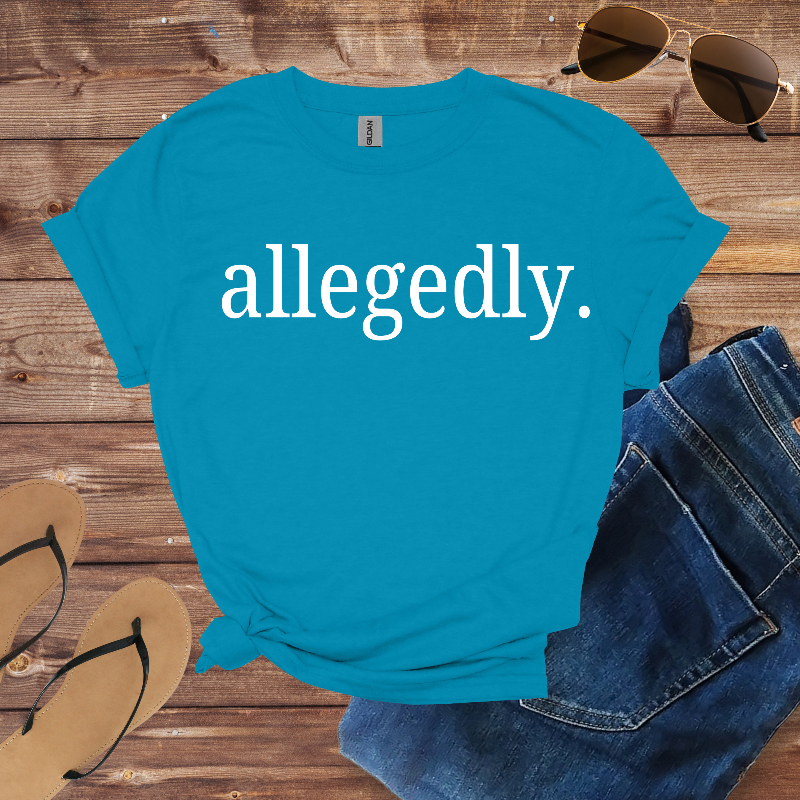 Blue t-shirt with 'allegedly.' text on a wooden surface with sunglasses, jeans, and flip-flops.