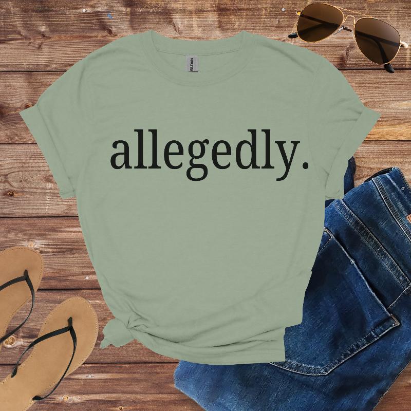 Green t-shirt with 'allegedly.' text on a wooden surface with jeans, sandals, and sunglasses.