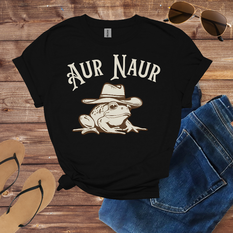 Black t-shirt with a frog wearing a cowboy hat and 'Aur Naur' text on a wooden surface with sunglasses and jeans.
