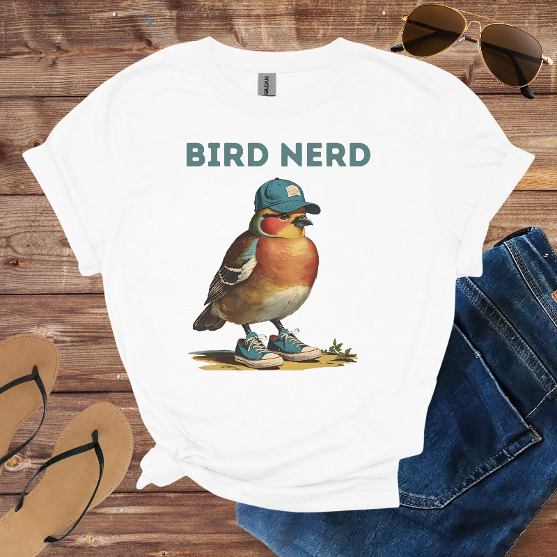 White t-shirt with a bird graphic and 'BIRD NERD' text on a wooden surface with sunglasses, jeans, and flip-flops.