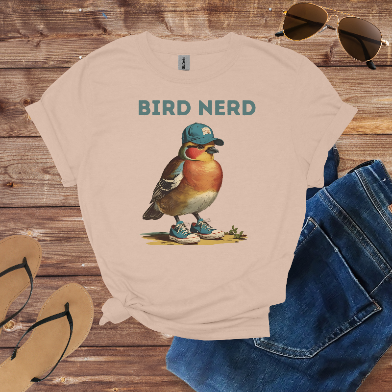Beige t-shirt with a bird graphic and 'Bird Nerd' text on a wooden surface with sunglasses, jeans, and flip-flops.