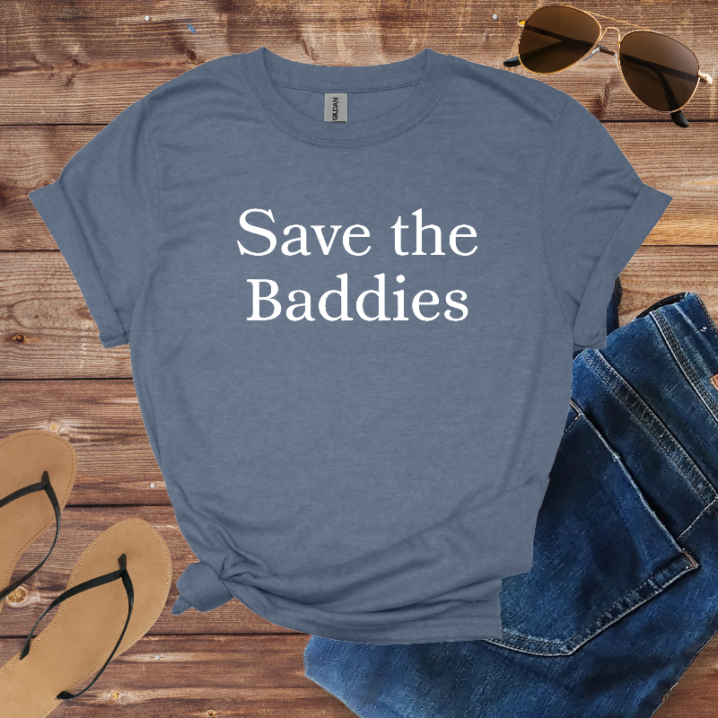 Blue t-shirt with 'Save the Baddies' text on a wooden surface with sunglasses, jeans, and sandals.