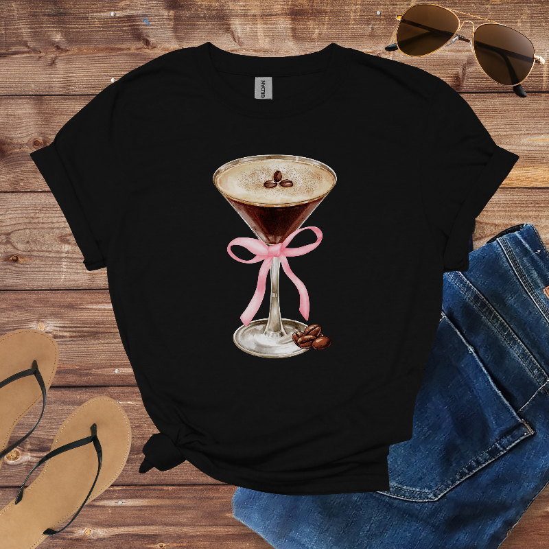 Black t-shirt with a coffee-themed design on a wooden surface with sunglasses, jeans, and sandals.