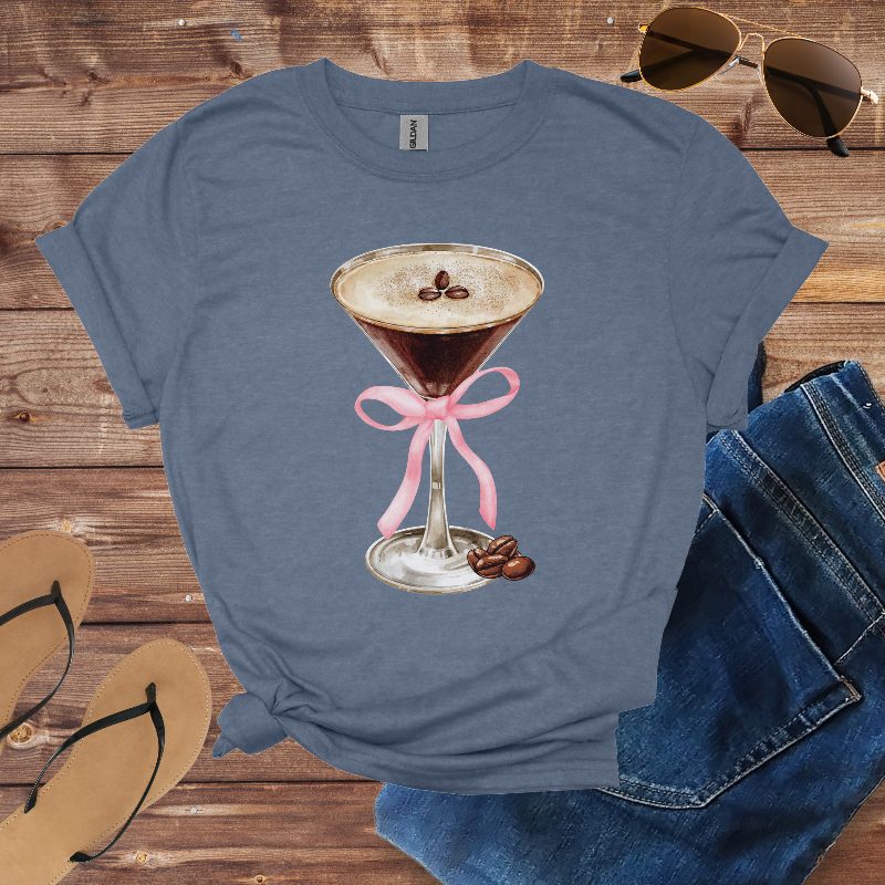 Blue t-shirt with a coffee-themed design on a wooden surface with sunglasses, jeans, and sandals.