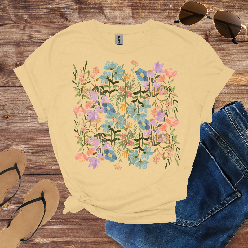 Beige t-shirt with floral design, sunglasses, sandals, and jeans on a wooden surface