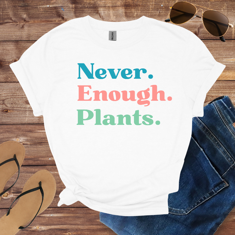 White t-shirt with 'Never. Enough. Plants.' text on a wooden surface with sunglasses, jeans, and flip-flops.