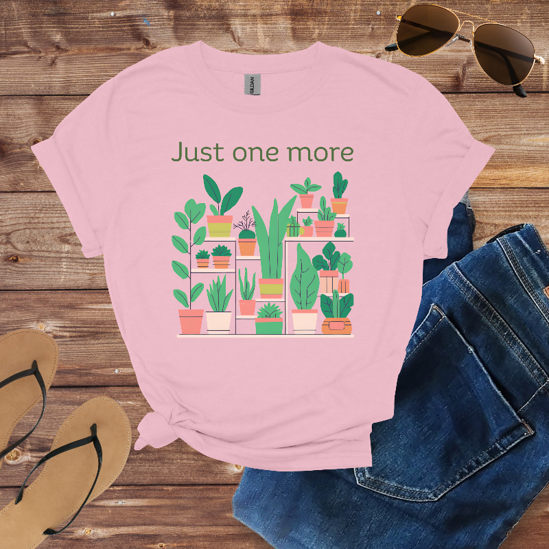 Pink t-shirt with plant graphic and text 'Just one more' on a wooden surface with sunglasses and jeans.
