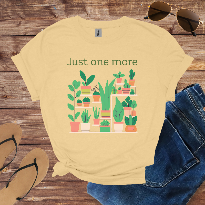 Beige t-shirt with plant graphic and text 'Just one more' on a wooden surface with sunglasses, sandals, and jeans.