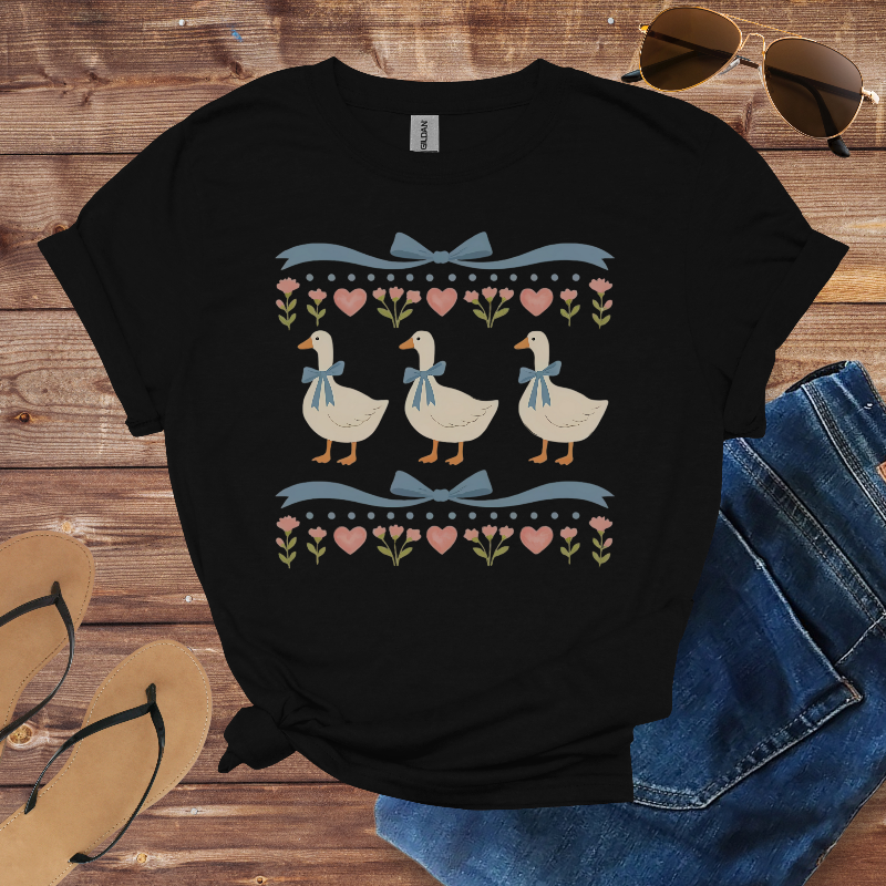 Black t-shirt with duck design on a wooden surface with sunglasses, jeans, and sandals.
