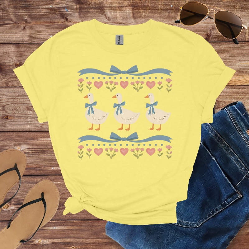 Yellow t-shirt with duck design on a wooden surface with sunglasses, jeans, and sandals.