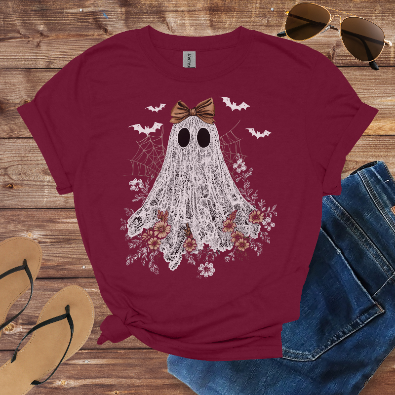 Maroon t-shirt with ghost design on a wooden surface with sunglasses, jeans, and sandals.