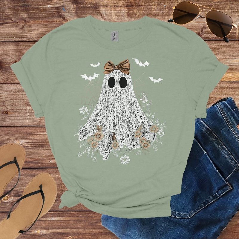 Green t-shirt with ghost design on a wooden surface with sunglasses, jeans, and sandals.
