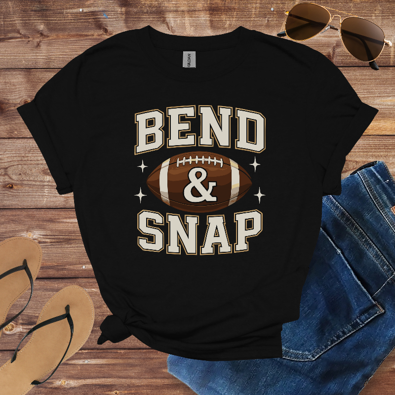 Black t-shirt with 'Bend & Snap' and football graphic on a wooden surface with sunglasses and jeans.