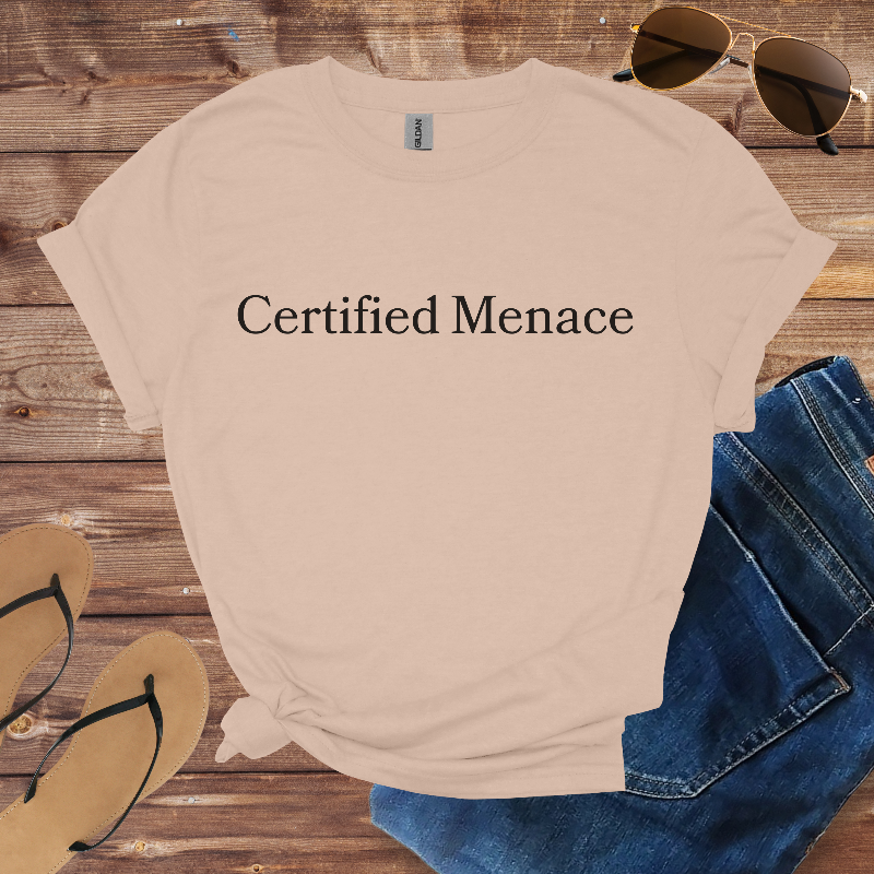 Beige t-shirt with 'Certified Menace' text on a wooden surface with sunglasses, jeans, and flip-flops.