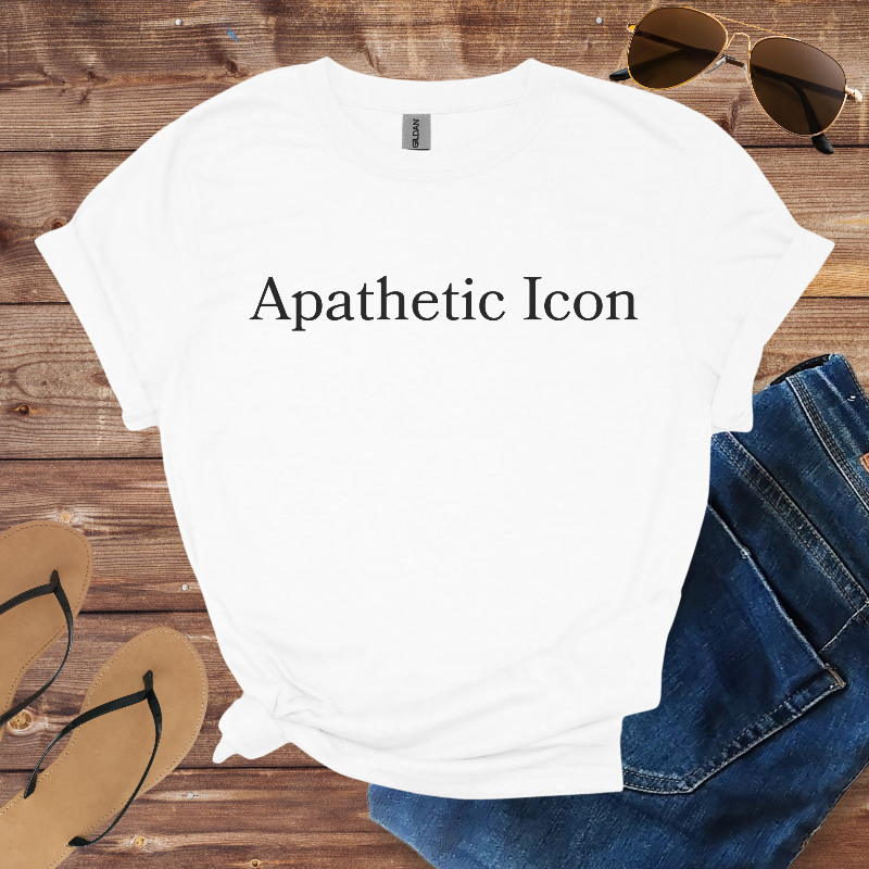 White t-shirt with 'Apathetic Icon' text, sunglasses, jeans, and sandals on a wooden surface