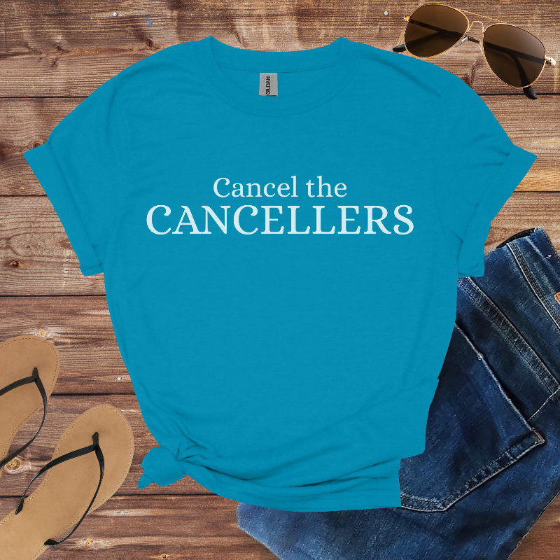 Blue t-shirt with 'Cancel the CANCELLERS' text on a wooden surface with sunglasses, jeans, and sandals.