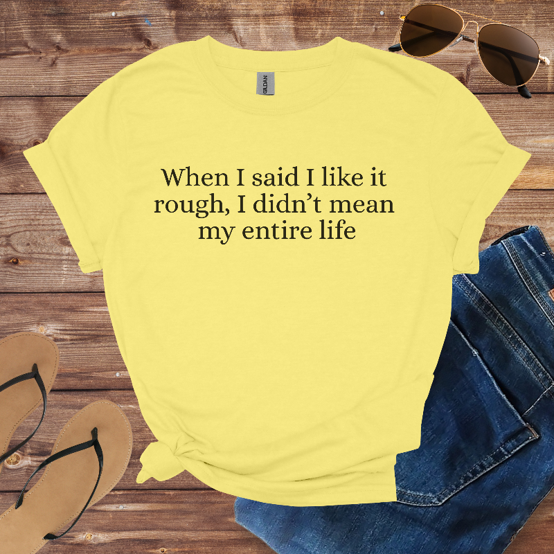 Yellow t-shirt with humorous text on a wooden surface with sunglasses, jeans, and sandals.