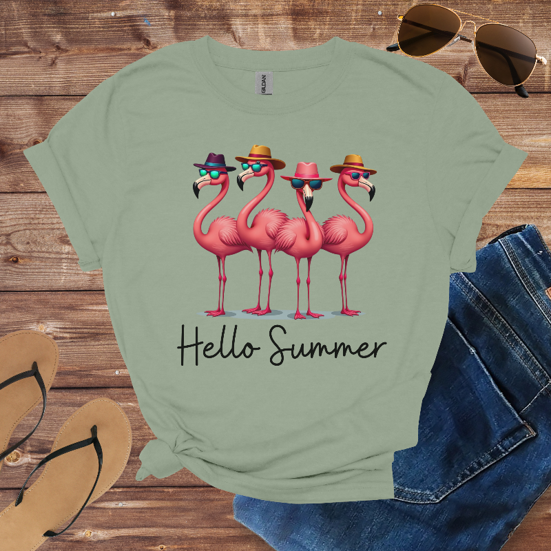 Green t-shirt with pink flamingo design and 'Hello Summer' text on a wooden surface with sunglasses and sandals.