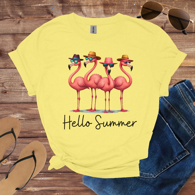 Yellow t-shirt with flamingo design and 'Hello Summer' text on a wooden surface with sunglasses and sandals.