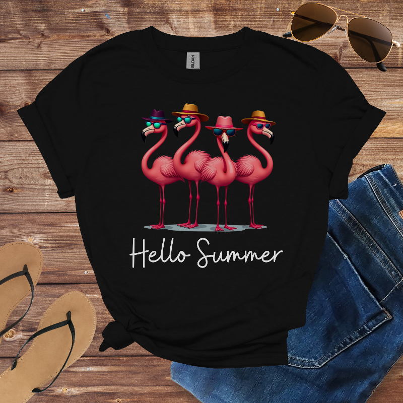 Black t-shirt with pink flamingo design and 'Hello Summer' text on a wooden surface with sunglasses, jeans, and sandals.