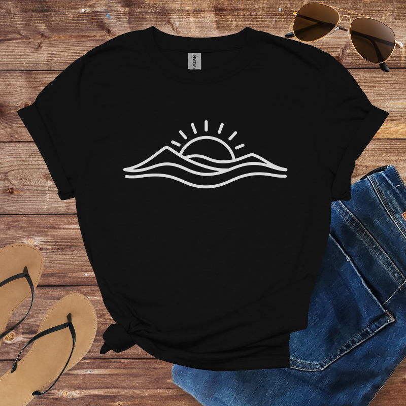 Black t-shirt with white graphic design on a wooden surface with sunglasses, jeans, and flip-flops.