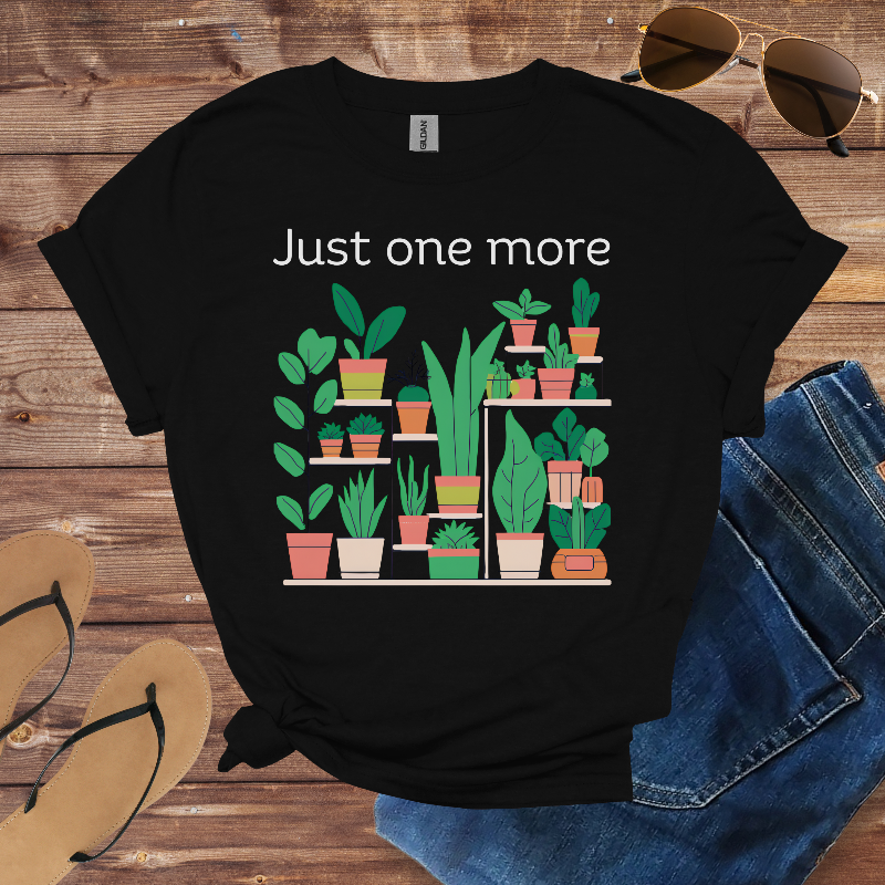 Black t-shirt with plant graphic and text 'Just one more' on a wooden surface with sunglasses, jeans, and sandals.