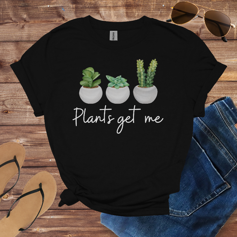 Black t-shirt with plant-themed design on a wooden surface with sunglasses, jeans, and sandals.