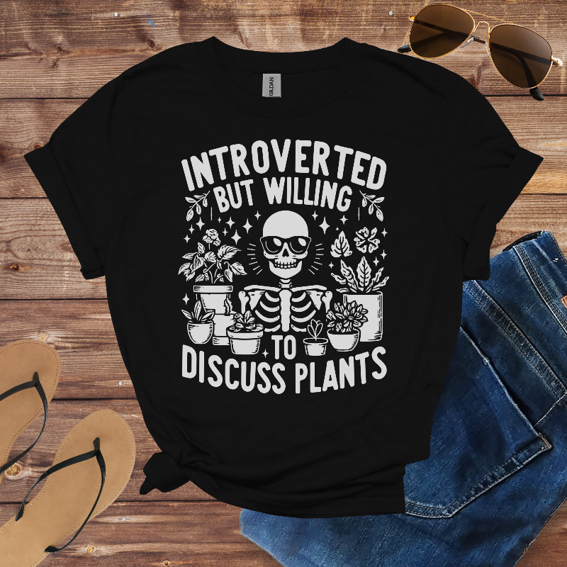 Black t-shirt with skeleton and plants design on a wooden surface with sunglasses and jeans.
