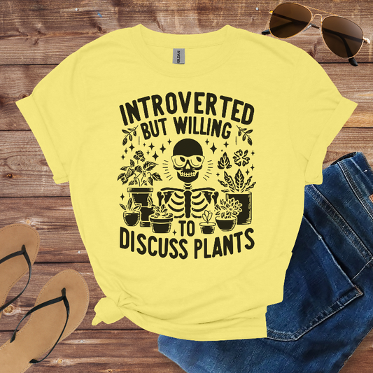 Yellow t-shirt with skeleton and plants design on a wooden surface with sunglasses and jeans.